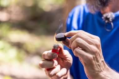Yanan bir çakmak tutan bir şifacı ve doğada tütsü yakmak için bir kömür diski hazırlıyor. Seçici odak