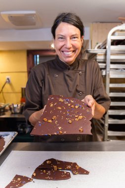 Gülen çikolatacı kadın elinde fındık ve çiçeklerle büyük siyah bir çikolata tutuyor. Seçici odak