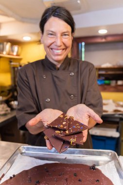 Çikolatacı kadın gülümsüyor ve elinde fındık ve çiçeklerle siyah çikolata parçaları tutuyor. Seçici odak