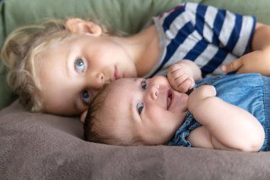 Uzun sarı saçlı ablası küçük kız kardeşine kanepede sarılıyor. Seçici odak