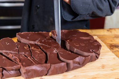 Çikolatacı büyük bir bıçakla tahta bir tahtada bir parça çikolata kesiyor. Seçici odak