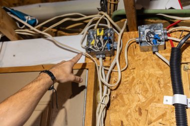 Elektrikçi tavan arası teftişi sırasında içinde kablolar olan bir elektrik kutusunu işaret ediyor. Seçici odak