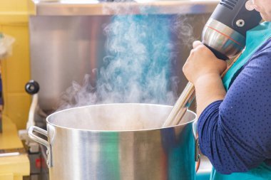 Şef, profesyonel bir mutfakta yemek hazırlarken büyük bir tencereye daldırma blenderi kullanıyor. Seçici odak