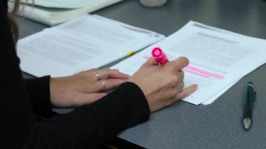 Kadın, pembe fosforlu kalemle yavaş çekimde, odaklanma ve konsantrasyon gösteren bir belgeye yazı vurguluyor. Seçici odak