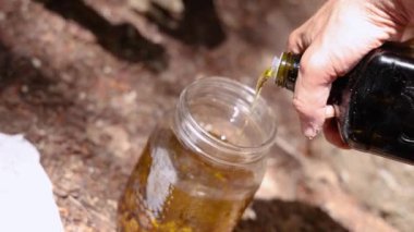 Bitkibilimci, reçinelerle dolu bir kavanoza yağ dökerek yağlı yağ hazırlama sanatını sergiliyor. Seçici odak