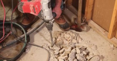 İnşaat işçisi kaya matkabını kullanıyor, ağır çekimde beton zemini kırıyor, yıkım sırasında toz ve enkaz oluşturuyor. Seçici odak