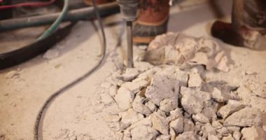 İnşaat işçisi matkap kullanıyor, betonu moloz yığınına çeviriyor. Yavaş çekim tozlu bir inşaat sahasında kesin delme hareketini yakalar. Seçici odak