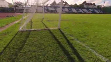 Yavaş çekim boş bir futbol kalesinin yanından süzülerek geçen bir kamerayı çeker. Sakin bir günde güneşli, parlak bir gökyüzünün altında.