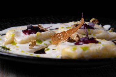 Peynirli ravioli ve siyah tabakta otlar.