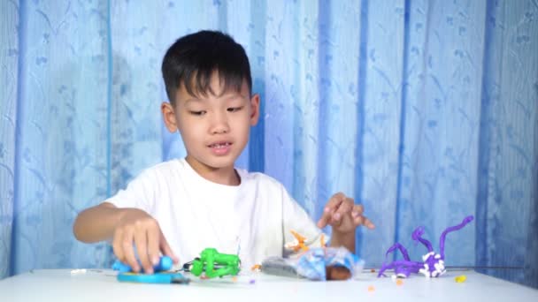Koncentrerad Asiatisk Pojke Sitter Och Gör Dockor Plast Ett Vitt — Stockvideo