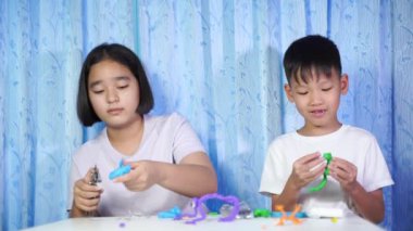 Çocuklar oyuncaklarla oynuyor, konsantre Asyalı kızlar ve oğlanlar evdeki beyaz bir masada plastik bebeklerden oyuncaklar yapıyor..