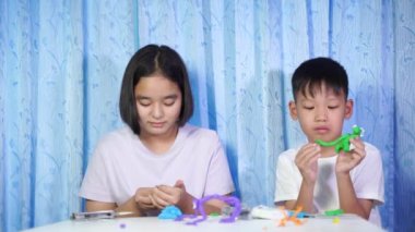 Çocuklar oyuncaklarla oynuyor, konsantre Asyalı kızlar ve oğlanlar evdeki beyaz bir masada plastik bebeklerden oyuncaklar yapıyor..