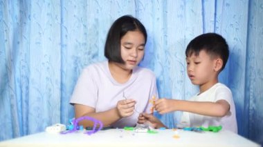 Çocuklar oyuncaklarla oynuyor, konsantre Asyalı kızlar ve oğlanlar evdeki beyaz bir masada plastik bebeklerden oyuncaklar yapıyor..