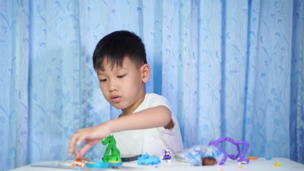 Koncentrovaný Asijský Chlapec Sedět Dělat Panenky Plasticinu Bílém Stole Domě — Stock video