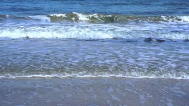 Kum plajına doğru yuvarlanan köpüklü dalgalar, derin mavi okyanus suyu ve köpüklü dalgalarla karşılaşan altın plaj. Turkuaz deniz dalgaları kumlu sahil şeridinde kırılıyor. 