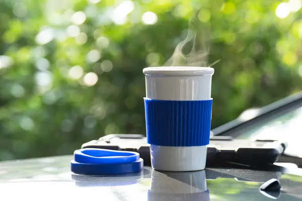 Hot ceramic white coffee cup with smoke placed outside the car dashboard at sunrise in the morning, in a natural background. Hot Coffee Drink Concept, selective focus, soft focus.
