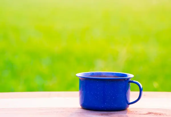 Kettle, blue enamel, and coffee mugs On an old wooden floor, Blurred background of rice fields at sunrise.