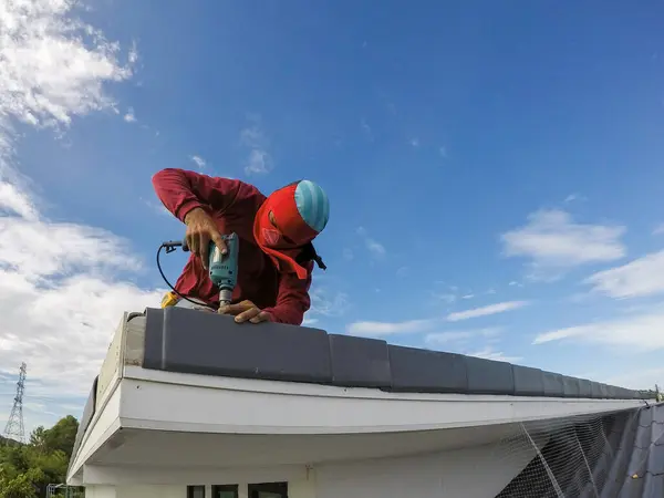 stock image male construction worker Using a drill Repairing a high roof on a house on a sunny day Blue sky with white clouds