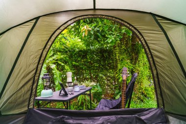 Çadırın içinden sabah ormanın içinde kamp çadırı kurmak için dinlenme ekipmanlarına bakıyorum.