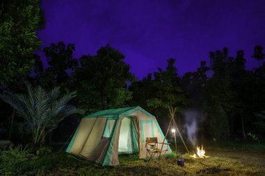 Geceleri kamp çadırları, eski kulübe çadırları, antika gaz lambaları, retro sandalyeler ve açık hava tesisleri olan bir grup kamp çadırı.