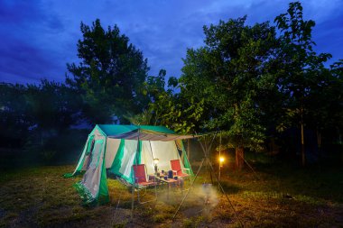 Geceleri kamp çadırları, eski kulübe çadırları, antika fenerler, retro sandalyeler ve ormandaki ahşap masalarda açık kahve yapma tesisleri.