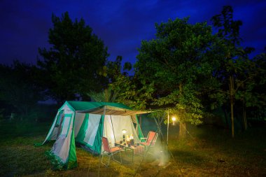 Geceleri kamp çadırları, eski kulübe çadırları, antika fenerler, retro sandalyeler ve ormandaki ahşap masalarda açık kahve yapma tesisleri.