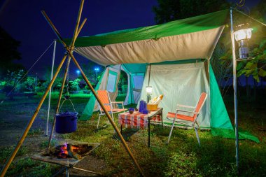 Geceleri kamp çadırları, eski kulübe çadırları, antika fenerler, retro sandalyeler ve ormandaki ahşap masalarda açık kahve yapma tesisleri.