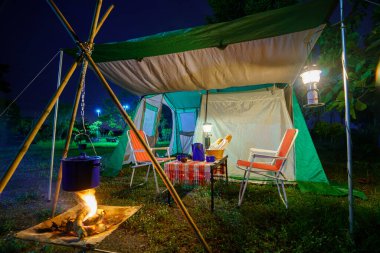 Geceleri kamp çadırları, eski kulübe çadırları, antika fenerler, retro sandalyeler ve ormandaki ahşap masalarda açık kahve yapma tesisleri.