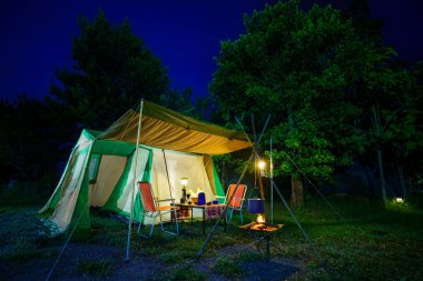 Geceleri kamp çadırları, eski kulübe çadırları, antika gaz lambaları, retro sandalyeler ve açık hava tesisleri olan bir grup kamp çadırı.