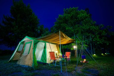 Geceleri kamp çadırları, eski kulübe çadırları, antika gaz lambaları, retro sandalyeler ve açık hava tesisleri olan bir grup kamp çadırı.