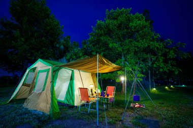 Geceleri kamp çadırları, eski kulübe çadırları, antika gaz lambaları, retro sandalyeler ve açık hava tesisleri olan bir grup kamp çadırı.