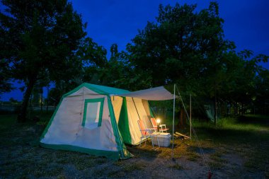 Geceleri kamp çadırları, eski kulübe çadırları, antika gaz lambaları, retro sandalyeler ve açık hava tesisleri olan bir grup kamp çadırı.
