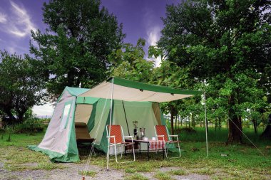 Kamp çadırları, eski kulübe çadırları, antika fenerler, retro sandalyeler ve ormandaki ahşap masalarda açık kahve yapma tesisleri.