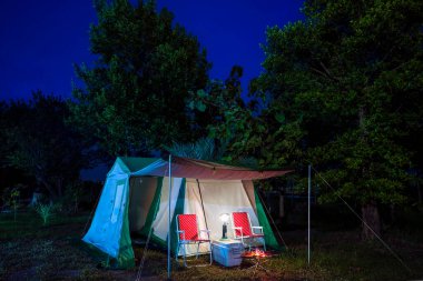 Geceleri kamp çadırları, eski kulübe çadırları, antika gaz lambaları, retro sandalyeler ve açık hava tesisleri olan bir grup kamp çadırı.