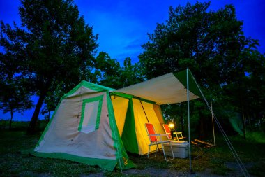 Geceleri kamp çadırları, eski kulübe çadırları, antika gaz lambaları, retro sandalyeler ve açık hava tesisleri olan bir grup kamp çadırı.