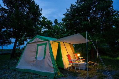 Geceleri kamp çadırları, eski kulübe çadırları, antika fenerler, retro sandalyeler ve ormandaki ahşap masalarda açık kahve yapma tesisleri.