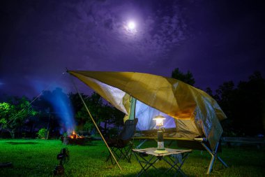 Geceleri ormanın içinde kamp çadırları. Gökyüzü arka planında ay ışığı, antik fenerler.