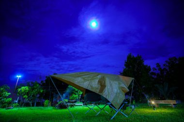 Geceleri ormanın içinde kamp çadırları. Gökyüzü arka planında ay ışığı, antik fenerler.