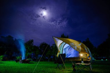 Geceleri ormanın içinde kamp çadırları. Gökyüzü arka planında ay ışığı, antik fenerler.