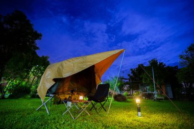 Geceleri ormanın içinde kamp çadırları. Gökyüzü arka planında ay ışığı, antik fenerler.