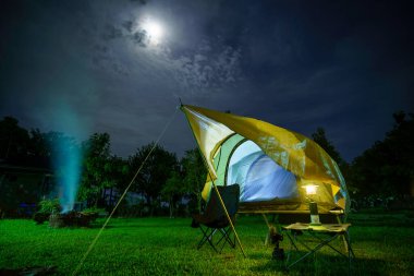 Geceleri ormanın içinde kamp çadırları. Gökyüzü arka planında ay ışığı, antik fenerler.