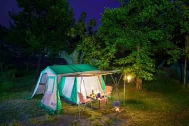 Geceleri kamp çadırları, eski kulübe çadırları, antika fenerler, retro sandalyeler ve ormandaki ahşap masalarda açık kahve yapma tesisleri.