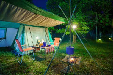 Geceleri kamp çadırları, eski kulübe çadırları, antika fenerler, retro sandalyeler ve ormandaki ahşap masalarda açık kahve yapma tesisleri.