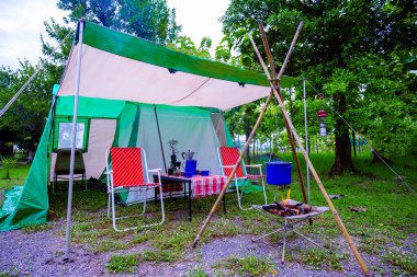 Geceleri kamp çadırları, eski kulübe çadırları, antika fenerler, retro sandalyeler ve ormandaki ahşap masalarda açık kahve yapma tesisleri.