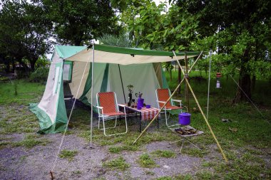 Kamp çadırları, eski kulübe çadırları, antika fenerler, retro sandalyeler ve ormandaki ahşap masalarda açık kahve yapma tesisleri.