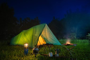 Ormanda yeşil ağaçlı kamp çadırı, geceleri ormanda kamp, yeşil çimlerin üzerinde küçük gaz lambası.