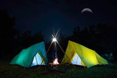 Ormanda yeşil ağaçlı kamp çadırı, geceleri ormanda kamp, yeşil çimlerin üzerinde küçük gaz lambası.