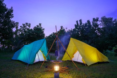 Ormanda yeşil ağaçlı kamp çadırı, geceleri ormanda kamp, yeşil çimlerin üzerinde küçük gaz lambası.