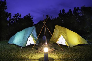 Ormanda yeşil ağaçlı kamp çadırı, geceleri ormanda kamp, yeşil çimlerin üzerinde küçük gaz lambası.