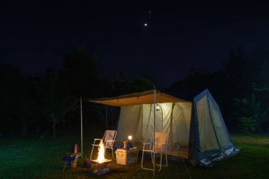 Geceleri kamp çadırları, antika kulübeler, antika gaz lambaları, retro sandalyeler ve ormandaki kamp alanındaki masalarda açık kahve yapma tesisleri olan bir grup kamp çadırı.